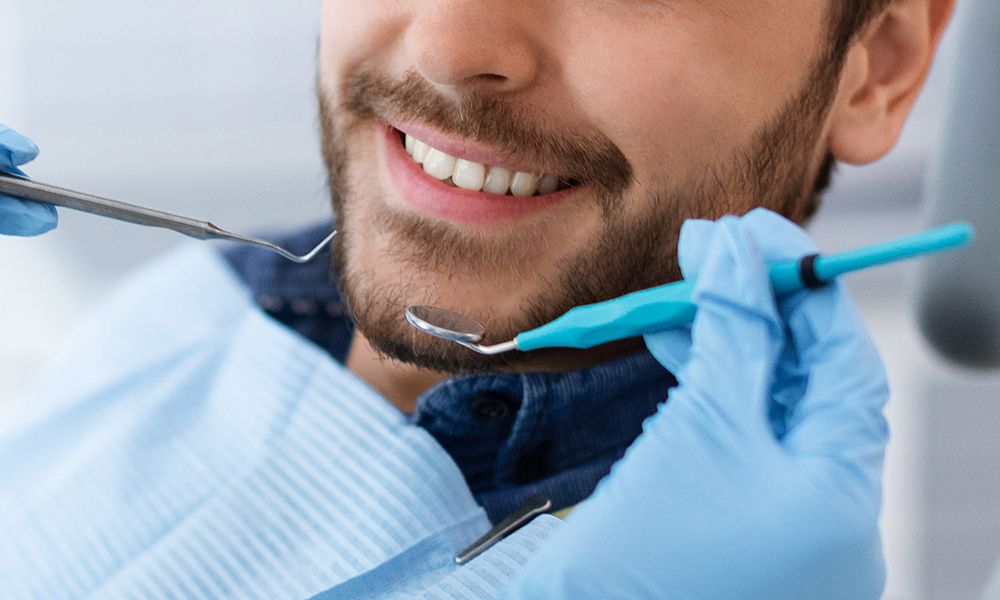 Primer plano de la sonrisa del paciente de la clínica dental y las manos del dentista sosteniendo instrumental.